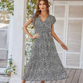 A woman wears a black and white floral summer dress with ruffle cap sleeves and short flutter sleeves