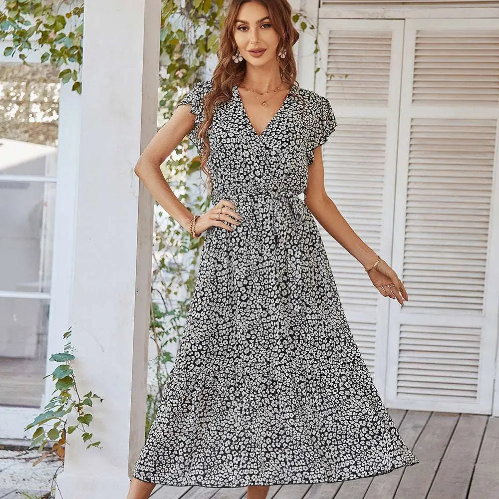 A woman wears a black and white floral summer dress with ruffle cap sleeves and short flutter sleeves