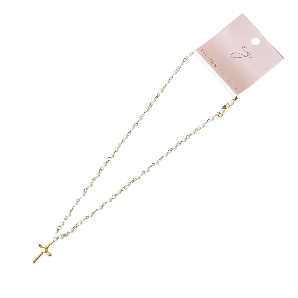 A delicate white pearl cabled rope cross pendant necklace with gold-tone accents on a pink Ellison Young tag