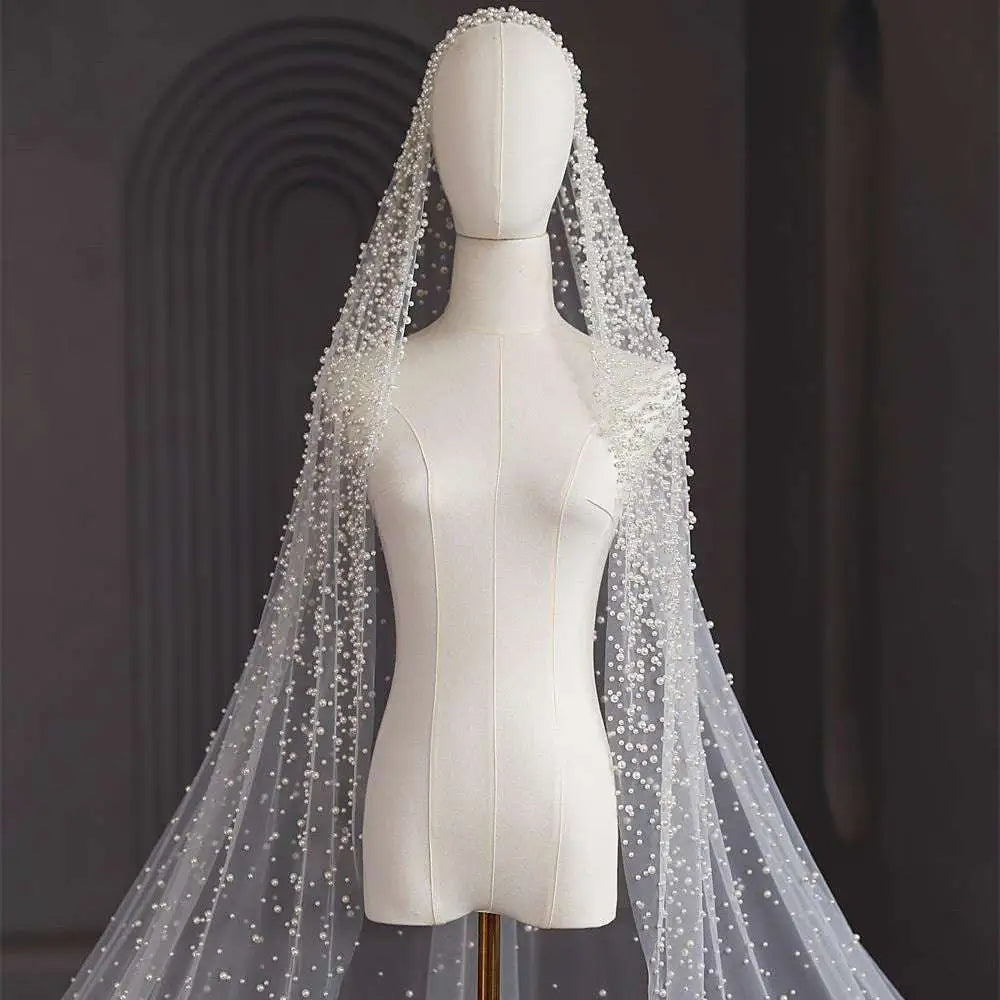 A delicate white pearl long luxury wedding veil with sheer flowing design and intricate beaded accents
