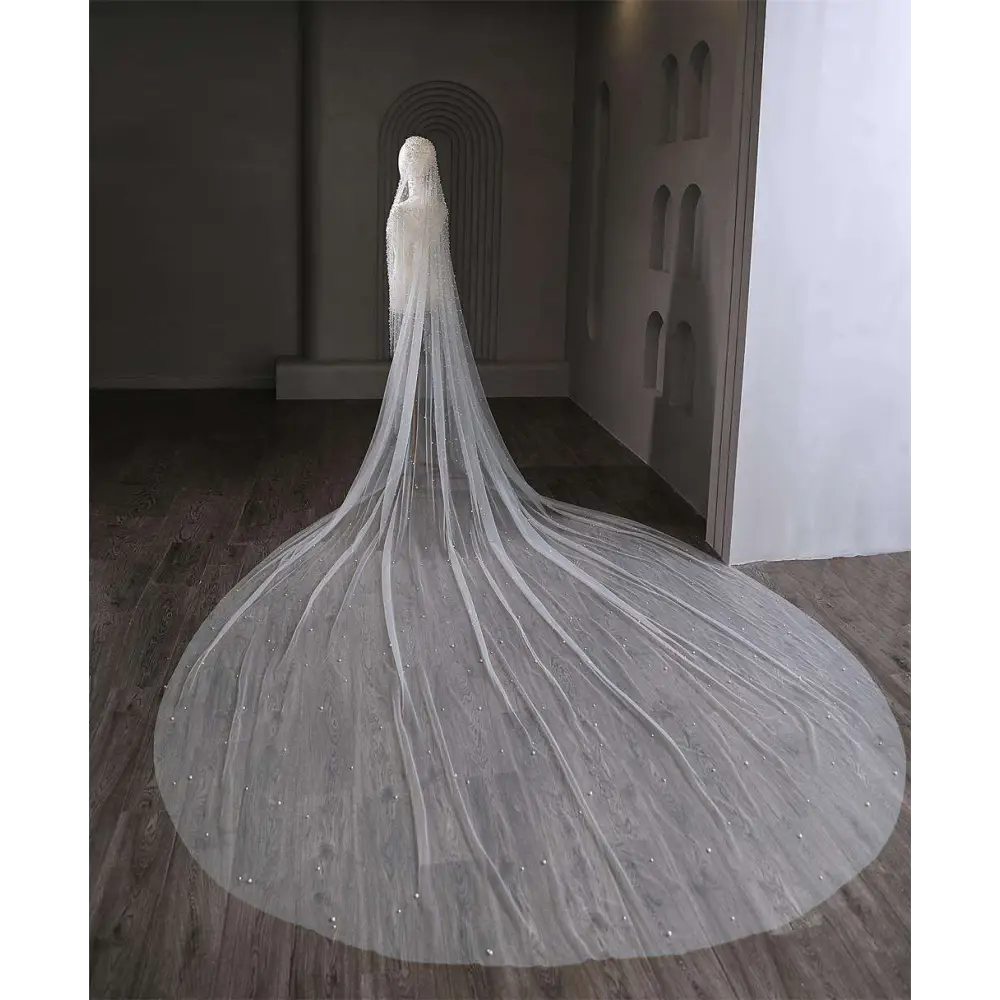 A flowing sheer white luxury wedding veil with delicate white pearl beaded accents cascading to the floor
