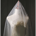 A delicate sheer white pearl wedding veil with scattered pearls and a dense cluster at the bust for long bridal cathedral use