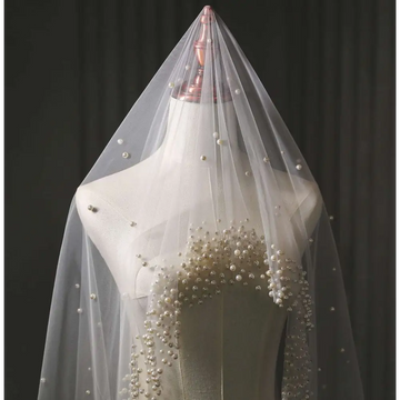 A delicate sheer white pearl wedding veil with scattered pearls and a dense cluster at the bust for long bridal cathedral use