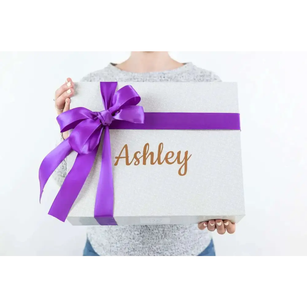 A shimmering silver gift box with a purple satin ribbon and personalized gold foil name for a skincare mom gift