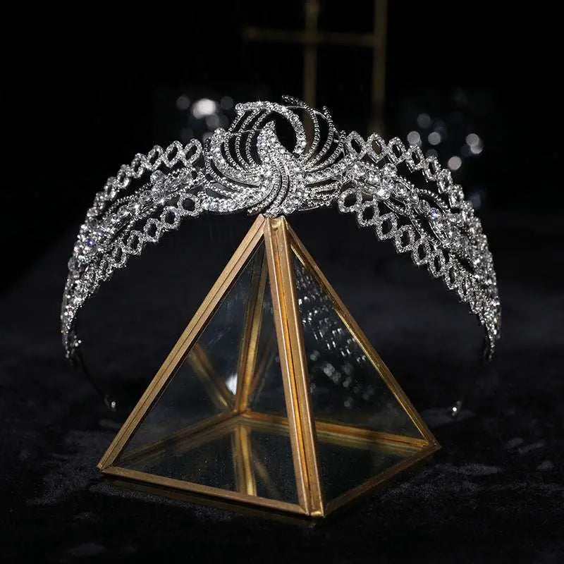 A sparkling silver rhinestone crown luxury bridal headdress with a phoenix motif on a gold triangular glass stand