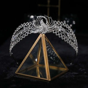 A sparkling silver rhinestone crown luxury bridal headdress with a phoenix motif on a gold triangular glass stand