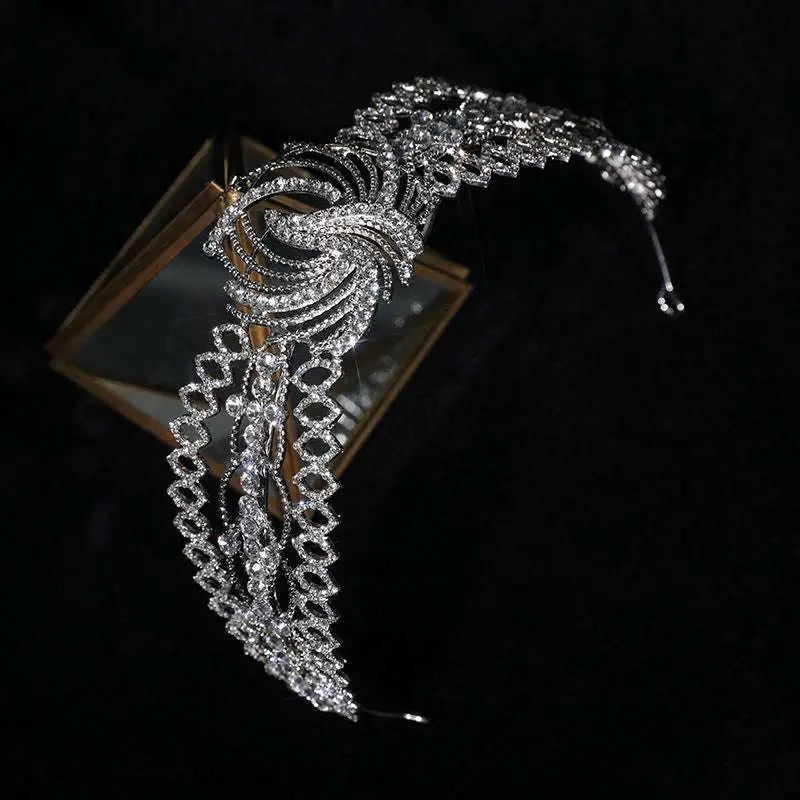 A sparkling silver rhinestone crown luxury bridal headdress with a phoenix motif on a gold triangular glass stand