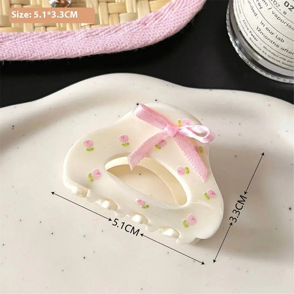 A white plastic small jaw clip with pink butterfly floral decals and a delicate pink ribbon bow for secure hold