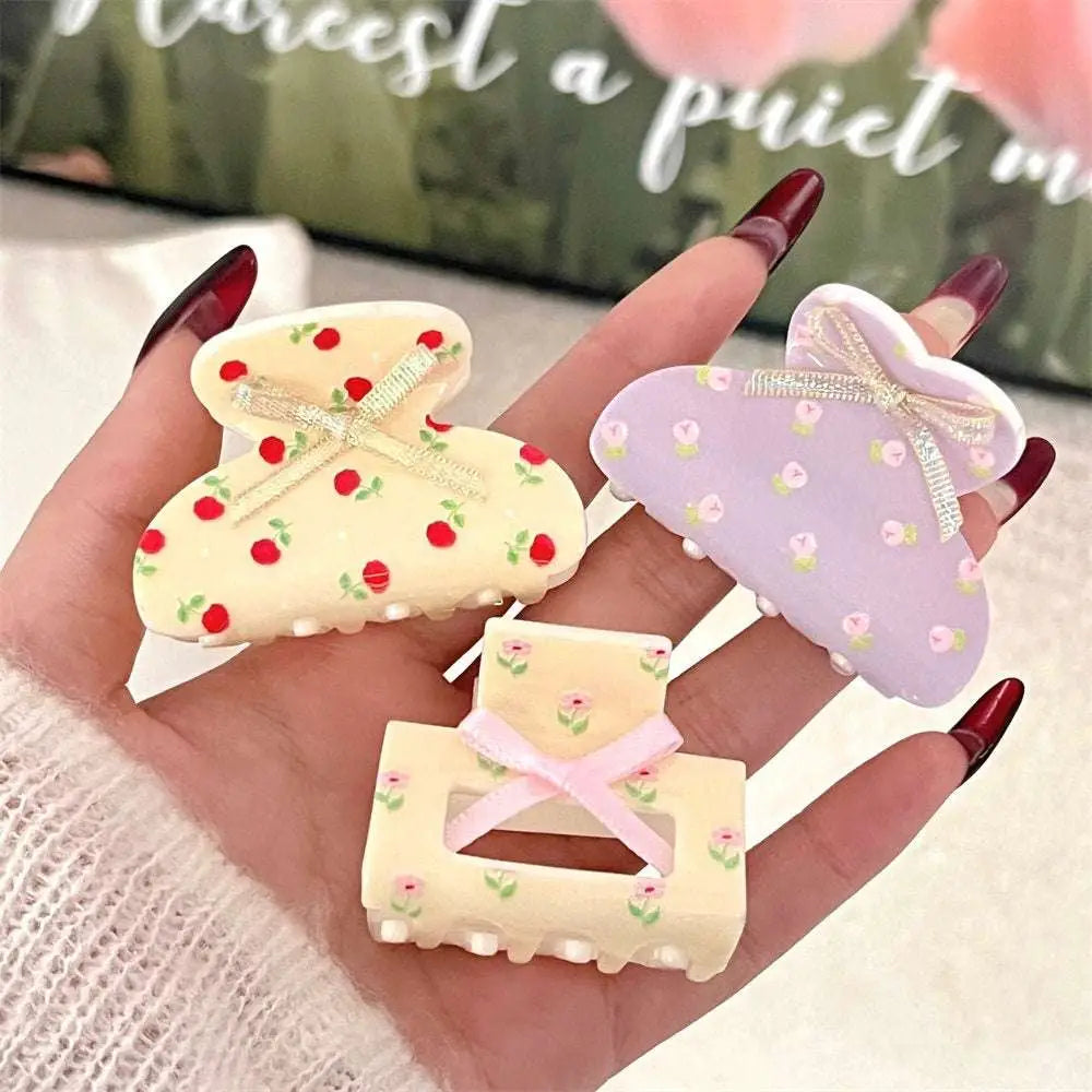 Three pastel-colored small jaw clips with pink butterfly floral patterns and decorative bows for secure hold