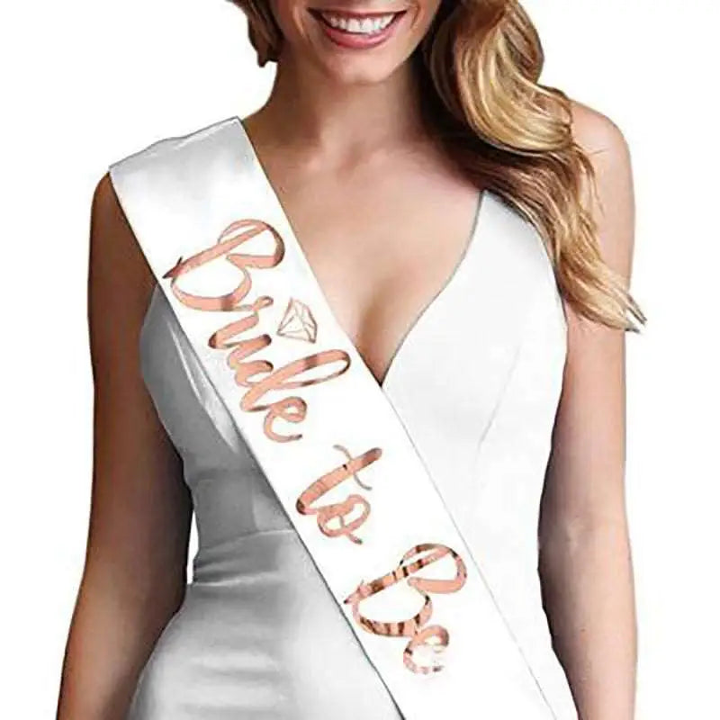 A white satin sash with rose gold foil bride cursive lettering and a diamond-shaped embellishment on popular tulle bridal veil