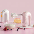 Pink handheld electric whisk with silver beaters and yellow accents featuring a clear base for luxury women’s fashion use