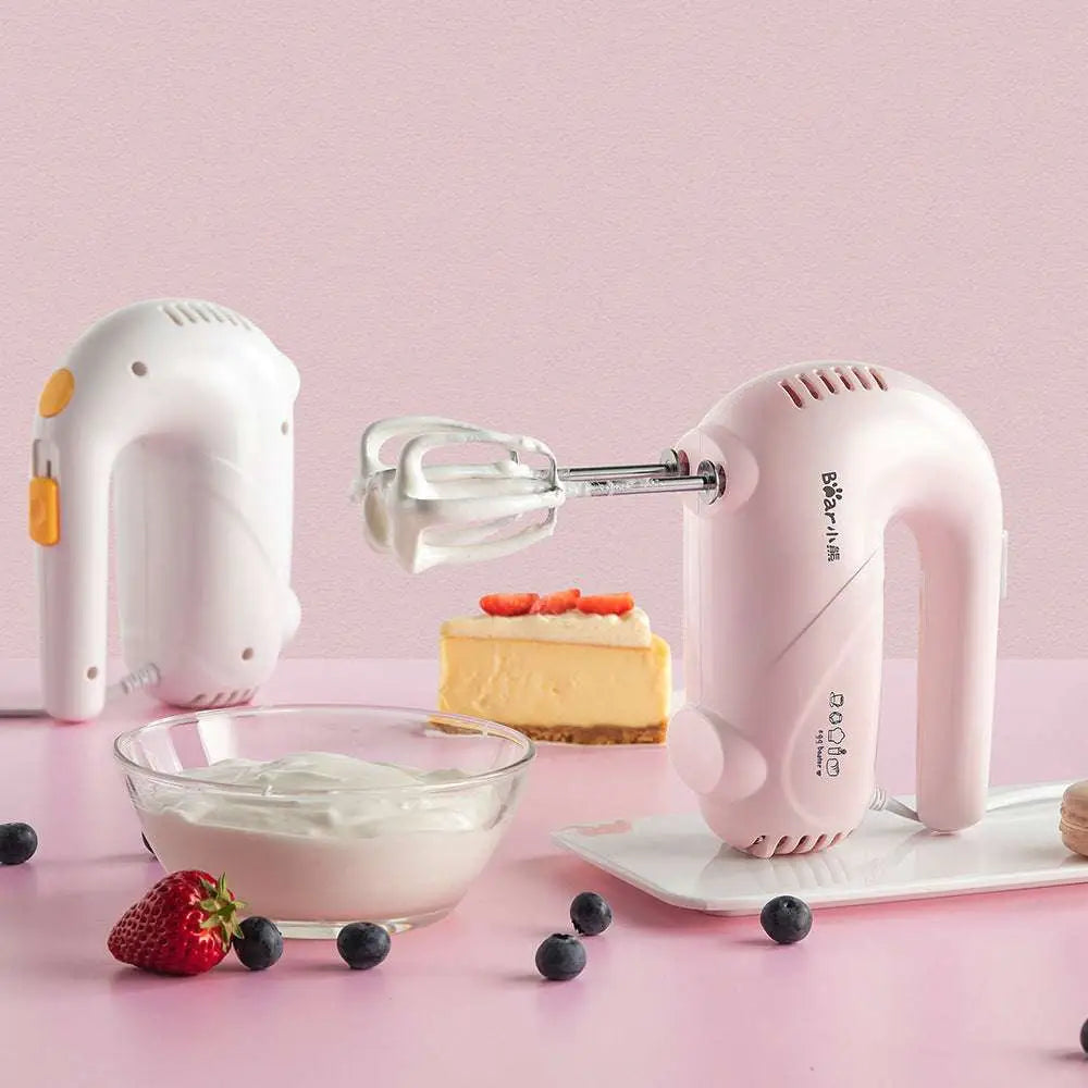 Pink handheld electric whisk with silver beaters and yellow accents featuring a clear base for luxury women’s fashion use