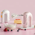 Pink handheld electric whisk with silver beaters and yellow accents featuring a clear base for luxury women’s fashion use
