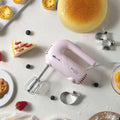 Pastel pink handheld electric whisk with metallic beaters and clear base designed for luxury women’s fashion lifestyle use
