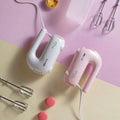 Pink handheld electric whisk with clear base and metallic beaters featuring brand logos for luxury women’s fashion use