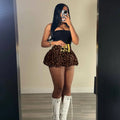 Gold-toned binoculars belt buckle complements pink leopard print pleated skirt with flared hem and polished finish