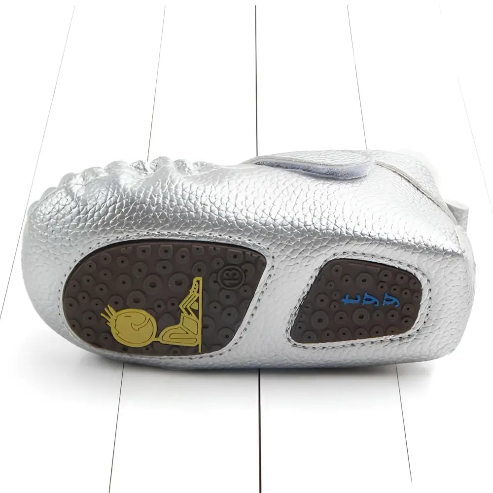 Silver textured leather baby shoes with brown sole and gold blue cartoon designs complement pink metallic tassel toddler shoes
