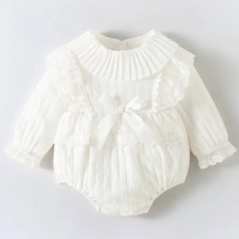 A delicate white newborn clothes jumpsuit with ruffled collar ribbed texture and lace trim on cuffs