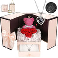 Pink moss bear with gold crown and heart necklace sits on red roses with white hydrangeas in elegant gift box