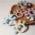Pastel pink silicone baby hand teether with soft textured surfaces and playful animal designs for infant use