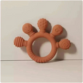 Pink silicone baby hand teether in terracotta color with four whimsical animal-shaped protrusions for teething relief