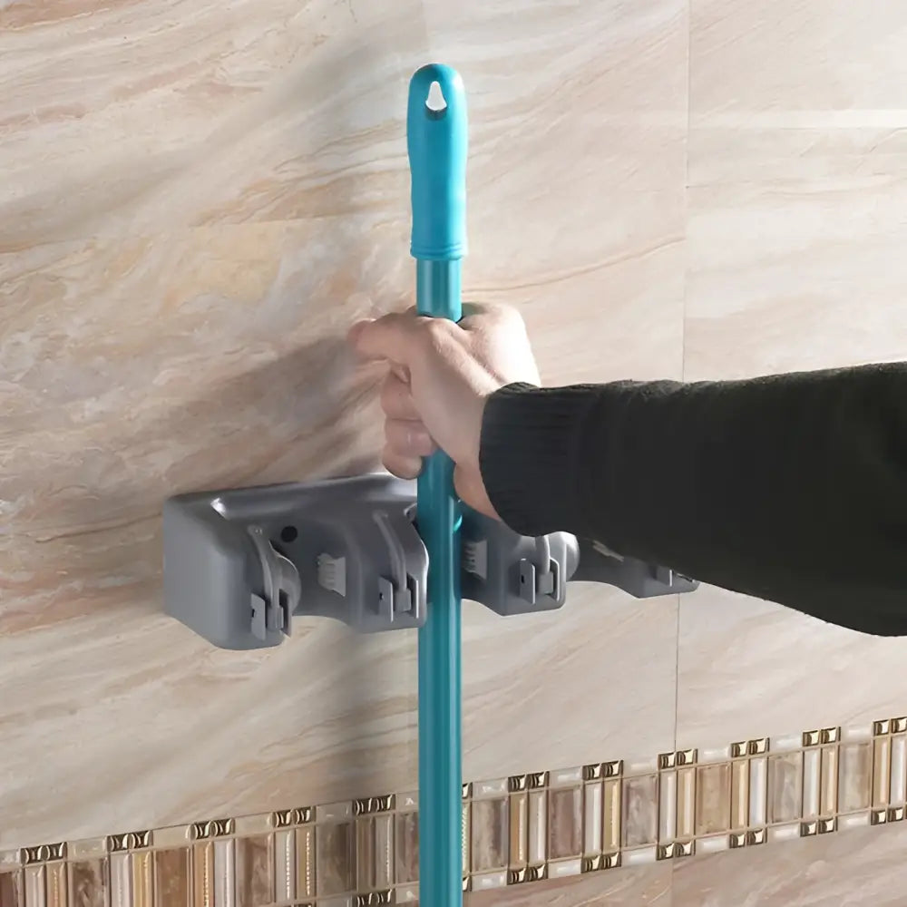 Teal plastic mop handle mounted in gray plastic mop hook wall hanging organizer rack for efficient storage