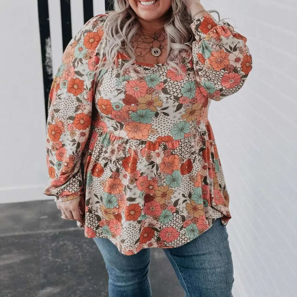 A plus size woman wears a casual loose floral chiffon peplum shirt in orange teal and brown on an off white background
