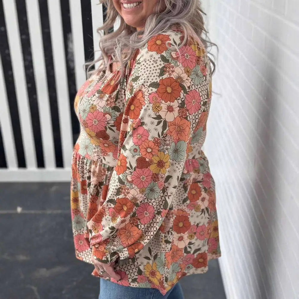 A plus size woman wears a casual loose floral chiffon peplum shirt in orange teal and brown on an off white background