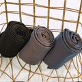 Three neatly rolled plus size fake translucent fleece lined tights in black gray and navy blue displayed on a golden basket