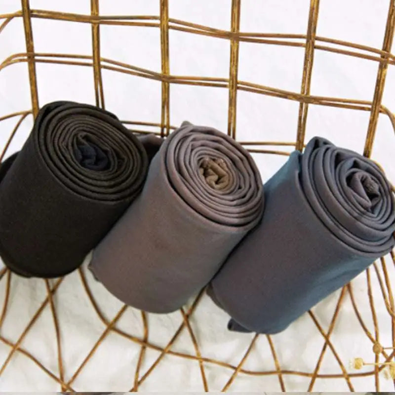 Three neatly rolled plus size fake translucent fleece lined tights in black gray and navy blue displayed on a golden basket