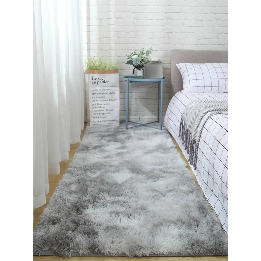 A plush gray shaggy carpet floor mat with soft fluffy texture lies on the floor in front of a bed