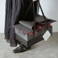 Black rectangular handheld flower box with clear window and red roses featuring a rolled gray paper lid and red bow knot
