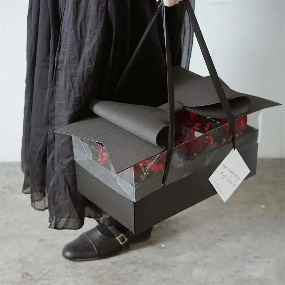 Black rectangular handheld flower box with clear window and red roses featuring a rolled gray paper lid and red bow knot