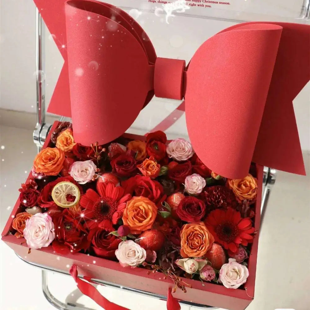 A handheld flower box with a clear window features a vibrant red bow knot and assorted roses gerbera daisies and citrus slices