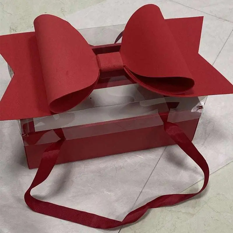 A vibrant red bow knot adorns a clear window handheld flower box with matching red fabric handles