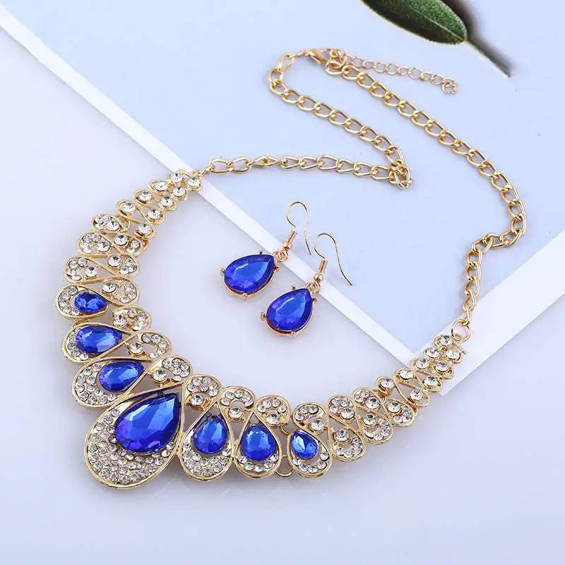 A glamorous red crystal teardrop american jewelry fashion set with gold tones, royal blue crystals, and matching earrings