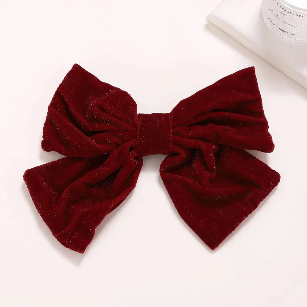 A plush deep red velvet bow spring clip accessory with a subtle glittery sheen for stylish hair decoration