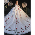 A flowing white wedding gown with red rose embroidery on the bodice and bride bra trailing featuring off-the-shoulder sleeves