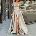 A flowing off-the-shoulder satin gown in soft beige with a high slit and structured bodice, styled as a swing split sleeveless gown