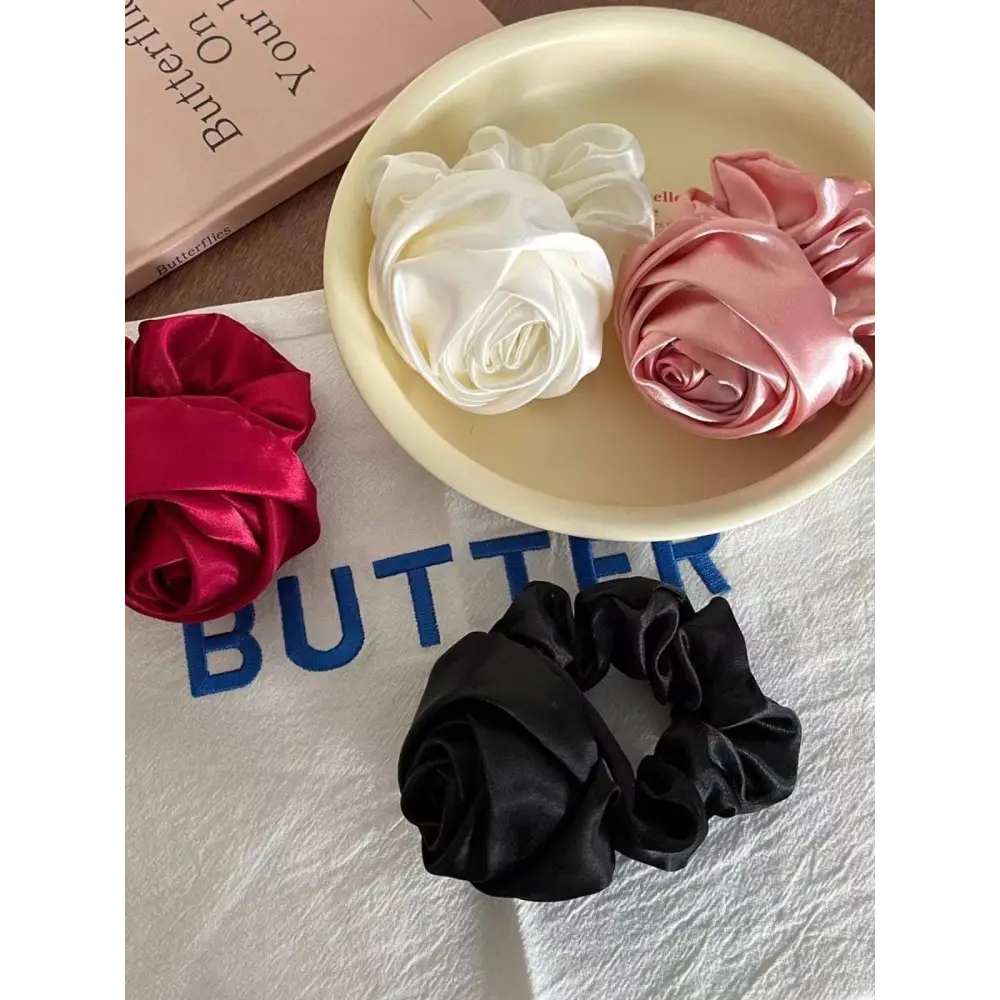 Three satin rose hair band scrunchies in white pink and black on a cream plate for bun ponytail advanced sense styling