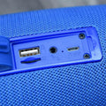 Blue textured fabric wireless bluetooth speaker with usb and 5v charging ports on the back panel featuring bluetooth audio