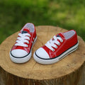Red toddler canvas casual shoes with white laces and rubber soles accented by black piping for children’s clothing