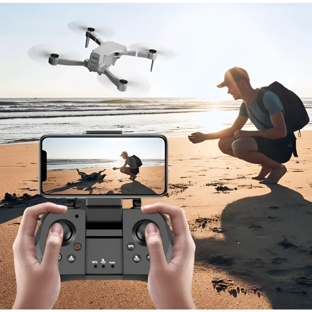 Gray folding drone with four propellers hovering above a sandy beach featuring mobile phone control and gps positioning