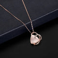 A delicate rose gold heart necklace with a pink triangular pendant surrounded by a diamond accented band