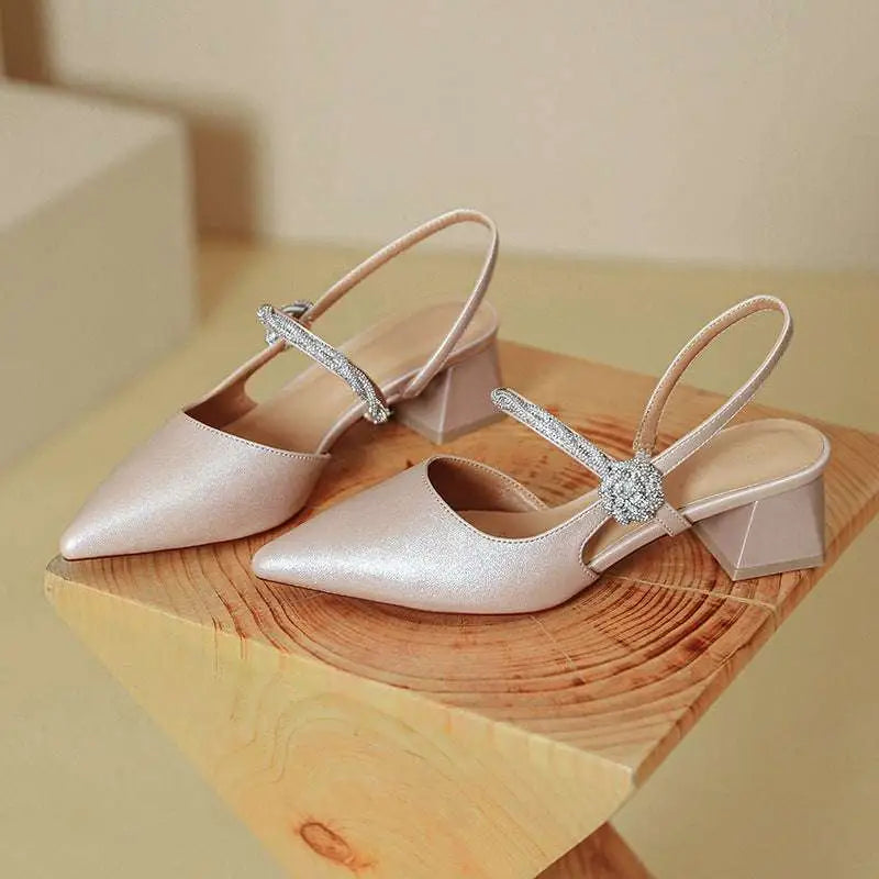 Rose gold satin pointed toe high heels featuring a chunky heel and crystal-embellished slingback strap