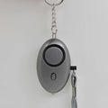 Silver oval-shaped personal security alarm with black button and textured grip attached to keychain for safety use