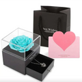 A vibrant turquoise preserved rose in a clear acrylic royal blue preserved rose jewelry gift box with a black base