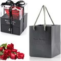 A vibrant red preserved rose in a clear acrylic box with black ribbon, paired with a dark gray rose jewelry gift bag