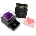 A vibrant purple preserved rose in a clear acrylic cube atop a royal blue preserved rose jewelry gift box
