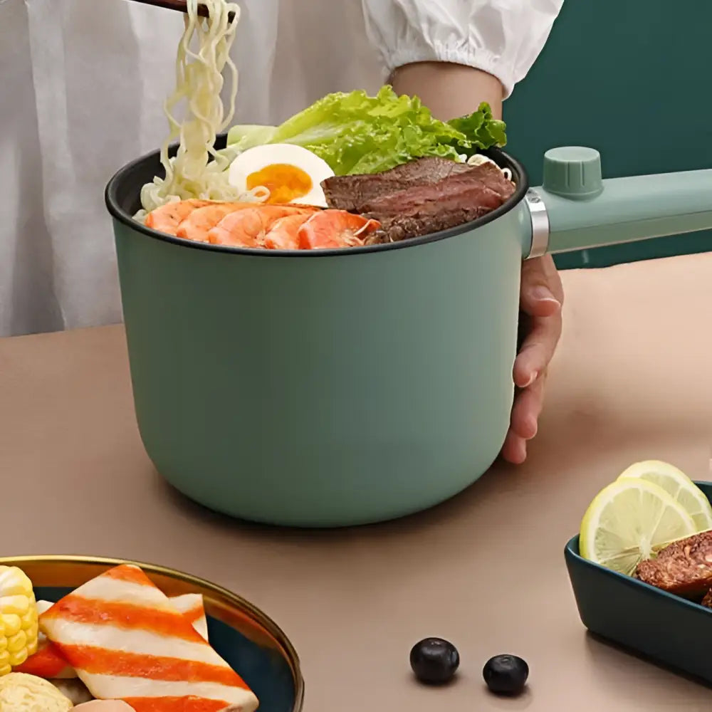 Sage green matte electric cooking pot with a handle and matching lid knob for versatile kitchen use